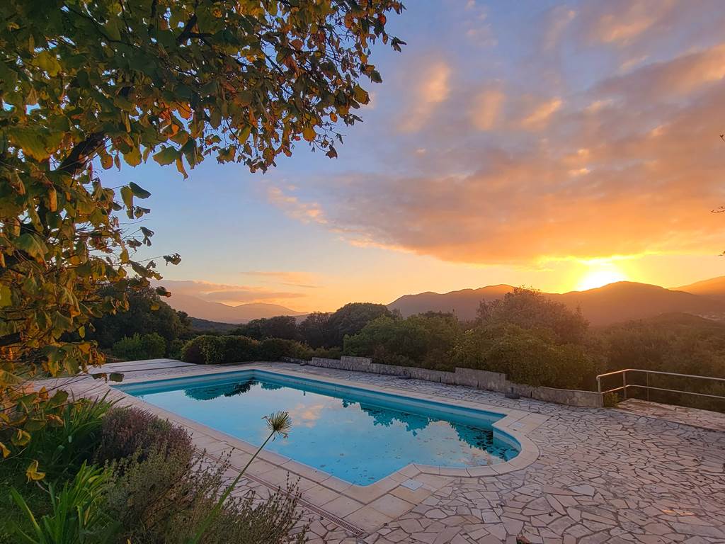 Piscine avec vue panoramique sur les montagnes corses embrasées par le soleil couchant.