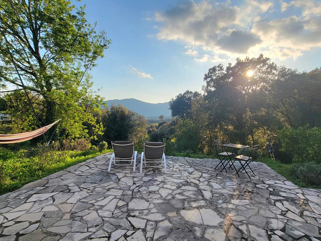Terrasse en pierre avec chaises longues offrant une vue imprenable sur le coucher de soleil corse.