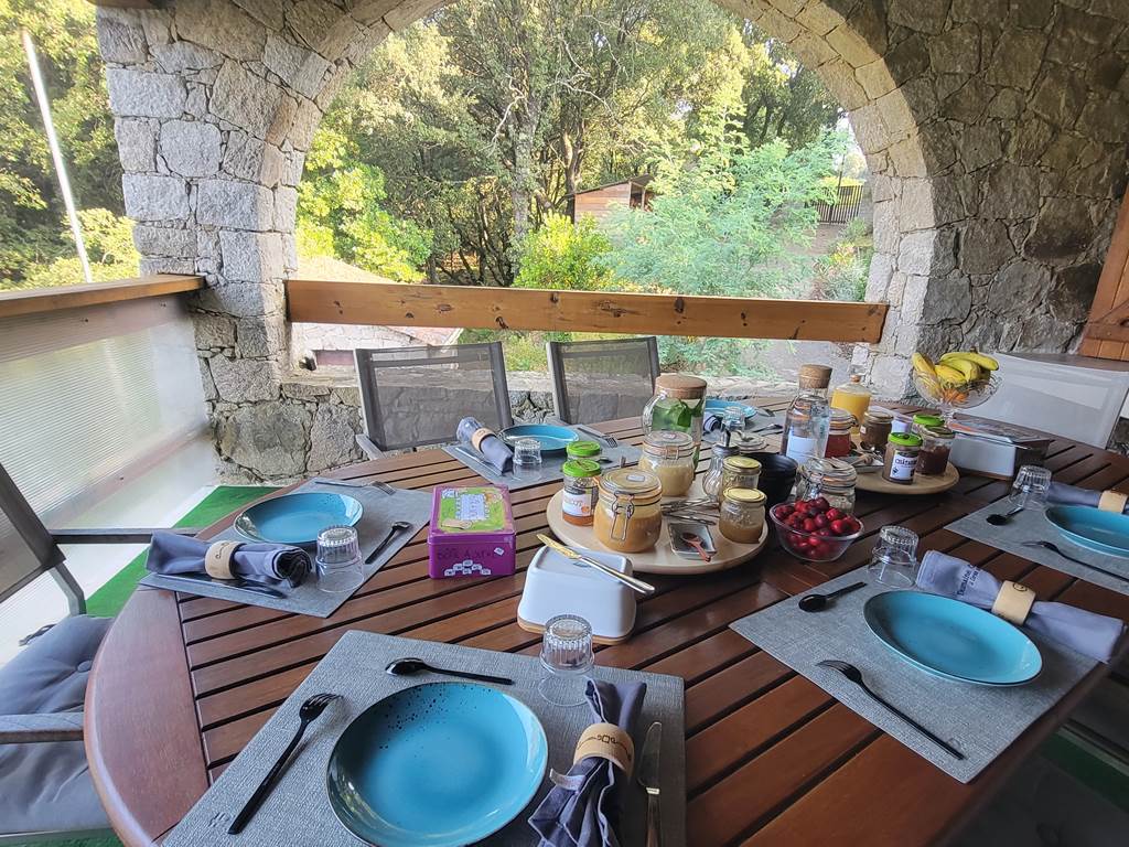 Table d'hôtes de charme dressée sur la terrasse en pierre pour un petit-déjeuner convivial en Corse.