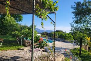 Espace détente ombragé dans le jardin arboré avec vue sur la piscine et la nature environnante.