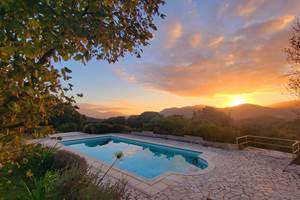 Piscine avec vue panoramique sur les montagnes corses embrasées par le soleil couchant.